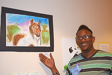 Shy Lofton stands before her drawings of majestic and loving animals.