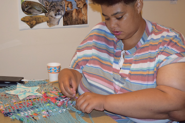 Seneca, an art student, continues to work on the collaborative project of a woven wall-hanging